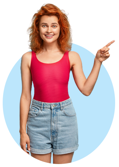Smiling young woman with ginger hair wearing a pink top and denim shorts pointing a finger to the right on a transparent background
